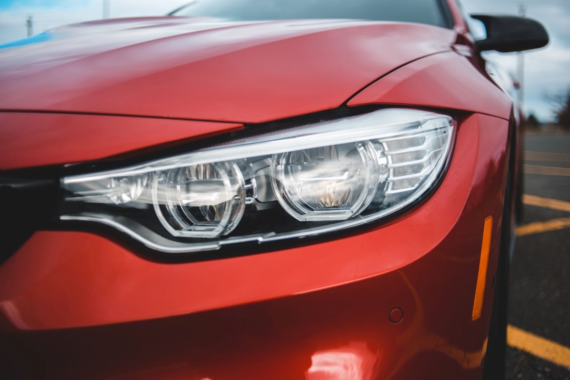 Frontpartie eines roten Autos, wobei der Fokus auf den rechten Frontscheinwerfer gerichtet ist. Die Scheinwerfer sind modern gestaltet, wahrscheinlich mit LED- oder Xenon-Technologie, und befinden sich in einem klaren und gut definierten Gehäuse, das nahtlos in die Karosserie des Fahrzeugs integriert ist. 