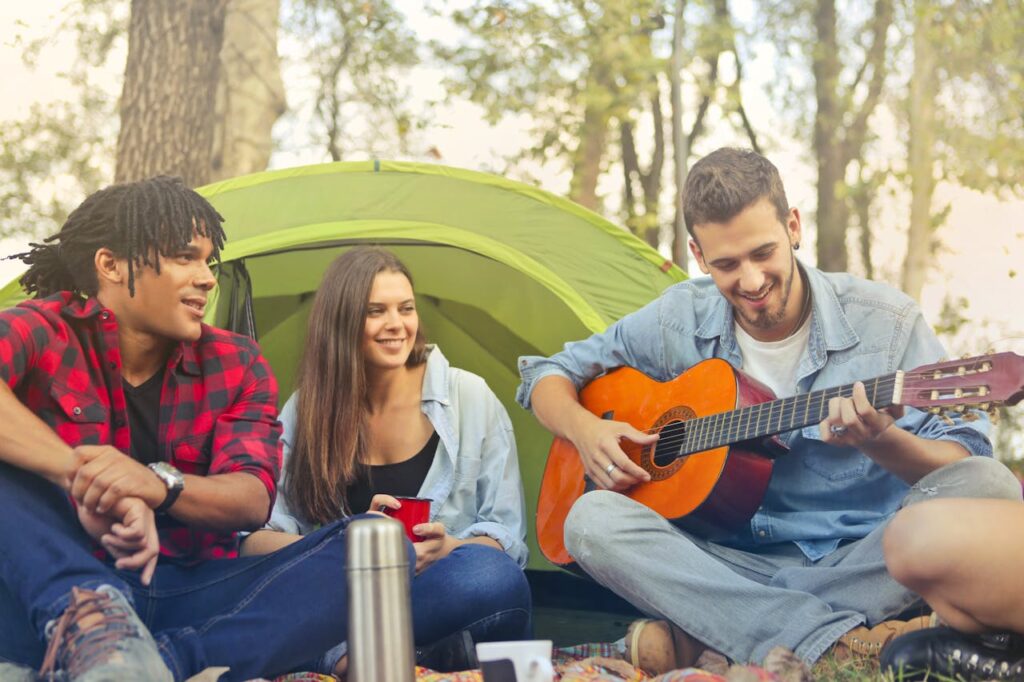 Drei junge Erwachsene genießen eine entspannte Campingzeit im Wald, ideal für Ausflüge mit einem geräumigen Reisemobil wie dem Ford Transit Custom.