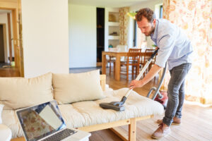 Hausmann versucht mit Staubsauger das Sofa zu reinigen