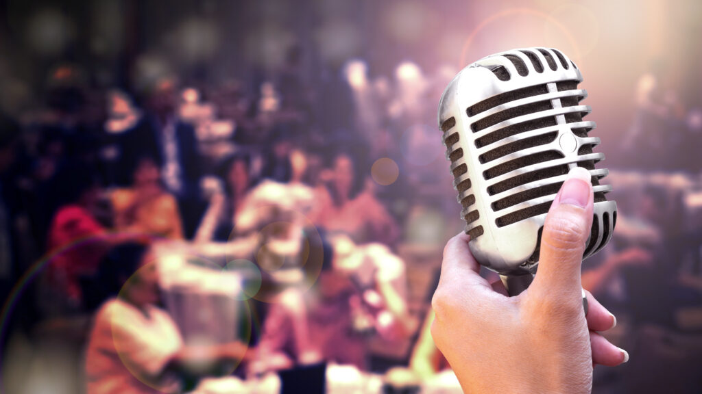 Mikrofon- und Gesangskonzept, Frauenhand hält Mikro vor Publikum