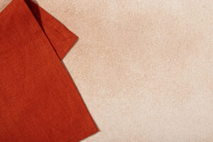 Orangefarbene Textil-Serviette auf Hintergrund aus beigem Baumwollputz.