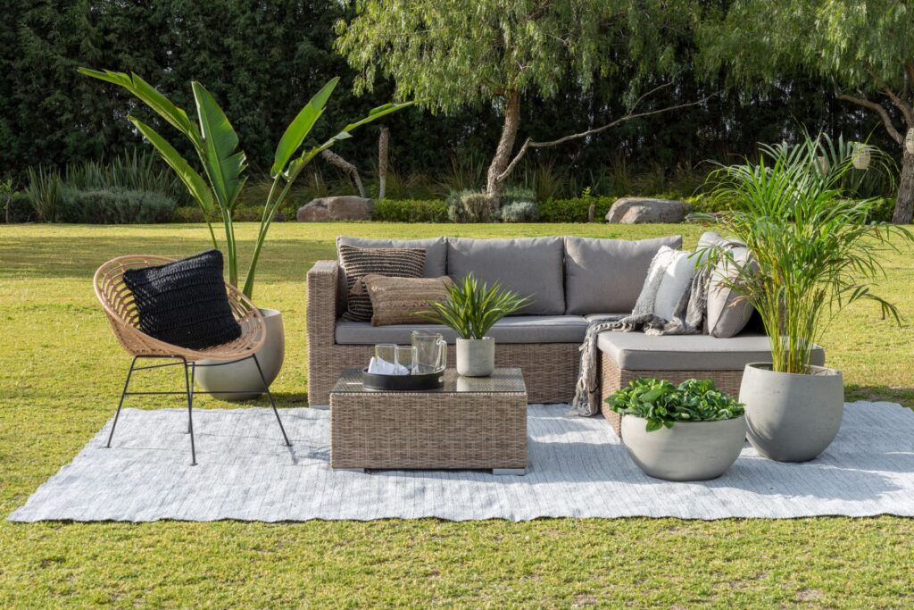 Eine moderne Außenterrasse mit einer bequemen Couch, Sesseln, dekorativen Kissen und üppigem grünen Gras