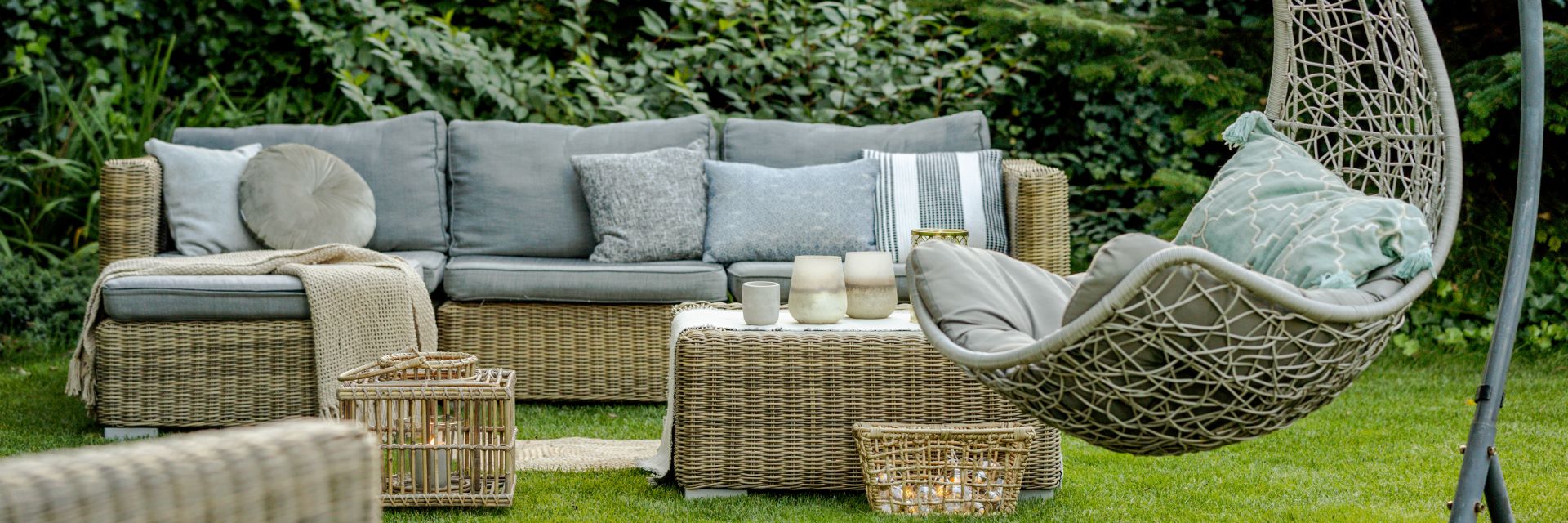 Bequeme Gartenmöbel aus Geflecht mit grauen Kissen in einem schönen Garten