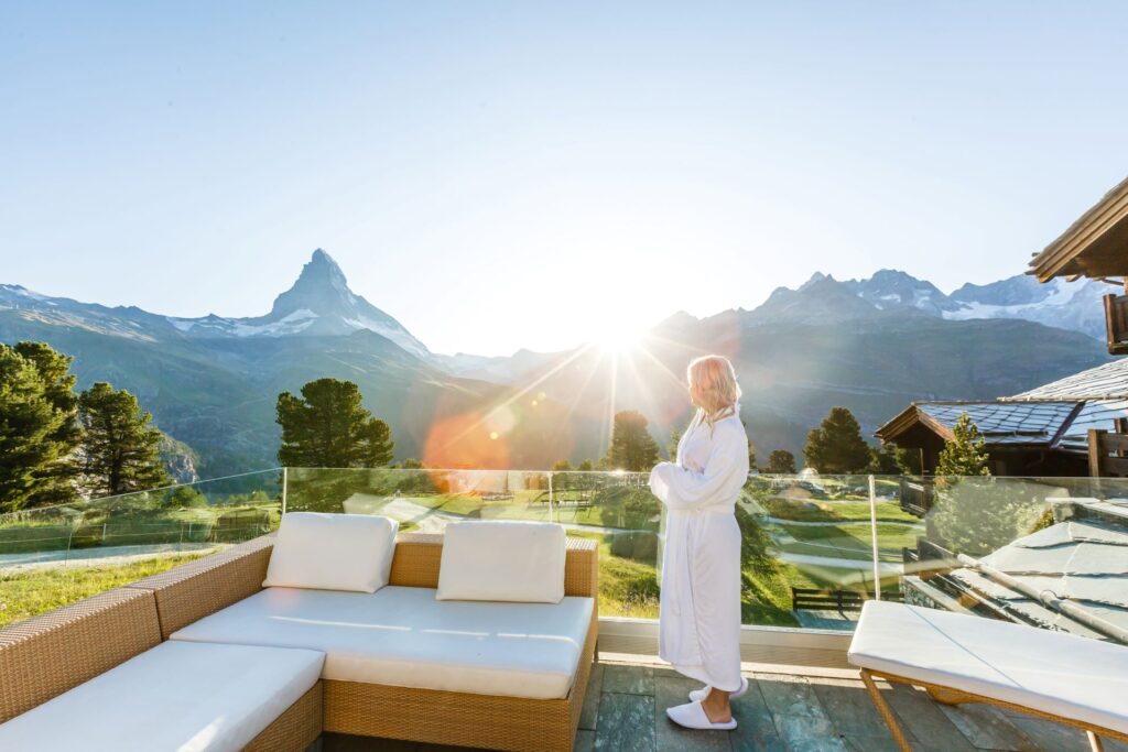 Frau im Bademantel mit Bergblick auf einer Terrasse.