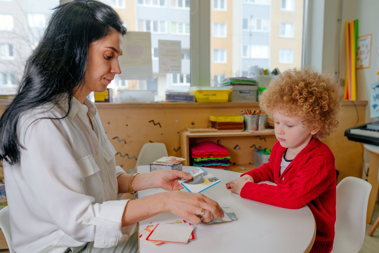 Therapeutin foerdert Kind mit roten Locken spielerisch mit Bildkarten – individuelle Sprachtherapie bei Logopaedie Herdecke